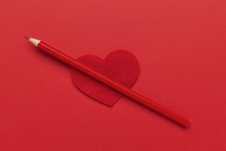 Red Pencil on Heart-Shaped Cutout: Symbol of Love and Creativity on Bold Red Backgroundの写真素材