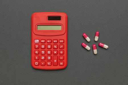 Red Calculator and Pink-White Capsules on Gray Background: Finance Meets Healthcare Conceptの写真素材