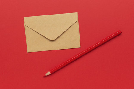 Minimalistic Red and Brown Composition with Envelope and Pencil on Red Backgroundの写真素材