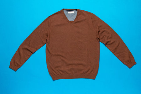 Brown V-Neck Sweater on Blue Background: Cozy Fashion Flat Lay for Stylish Wardrobe Inspirationの写真素材