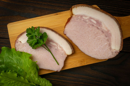 Sliced Ham on Wooden Board with Fresh Parsley and Lettuce on Dark Rustic Backgroundの写真素材