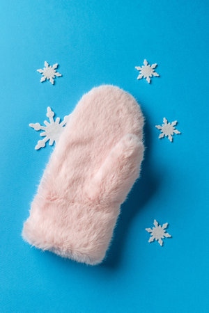 Soft Pink Winter Mitten Surrounded by Snowflakes on a Vibrant Blue Backgroundの写真素材