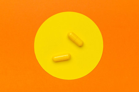 Yellow Capsules on Orange and Yellow Circle Background: Minimalist Health and Wellness Conceptの写真素材
