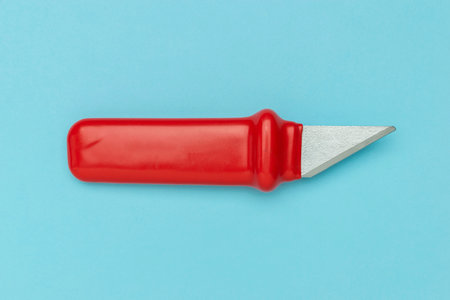 Red Handle Utility Knife on Light Blue Background Reflecting Minimalist Design in Stock Photographyの写真素材