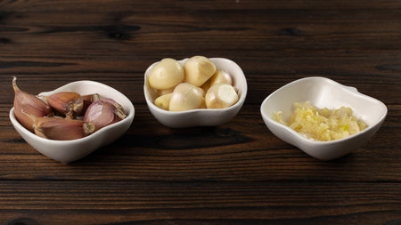 Fresh Whole, Peeled, and Minced Garlic in Heart-Shaped Bowls on Rustic Wooden Tableの写真素材