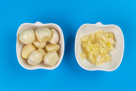 Fresh Garlic Cloves and Minced Garlic in Bowls on Blue Backgroundの写真素材
