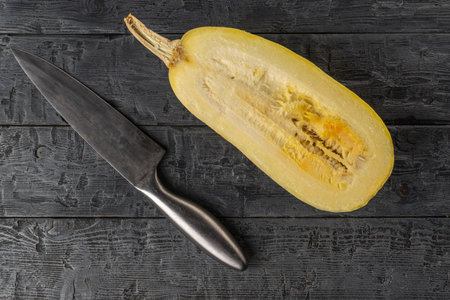 Top View of Fresh Spaghetti Squash Halved with Knife on Rustic Wooden Surfaceの写真素材