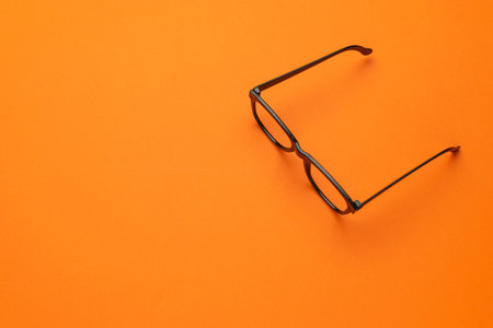 Minimalist Black Glasses on Vibrant Orange Background for Modern Design Conceptsの写真素材