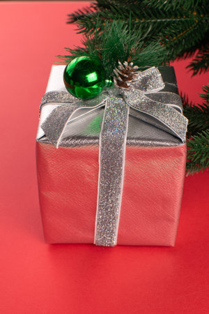Festive Gift Box with Silver Ribbon and Green Ornament on Red Holiday Backgroundの写真素材