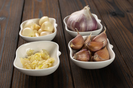 Garlic on Wooden Table: Cloves, Bulbs, and Minced Variations in Ceramic Bowls for Cooking Inspirationの写真素材