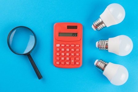 Energy Efficiency Concept with Calculator, Magnifying Glass, and LED Bulbs on Blue Backgroundの写真素材