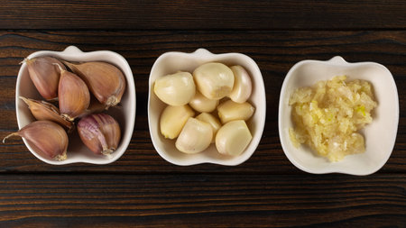 Fresh Garlic Display: Whole, Cloves, and Minced in Ceramic Dishes on Wooden Backgroundの写真素材