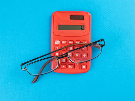 Red Calculator with Glasses on Blue Background: Symbol of Calculation and Vision in Businessの写真素材