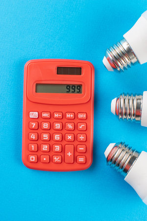 Red Calculator with 999 Display Surrounded by LED Light Bulbs on Blue Backgroundの写真素材