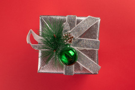 Christmas Gift Box Wrapped in Silver with Green Ornament on Red Background for Holiday Seasonの写真素材