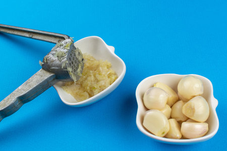 Freshly Minced Garlic with Garlic Press on Blue Backgroundの写真素材