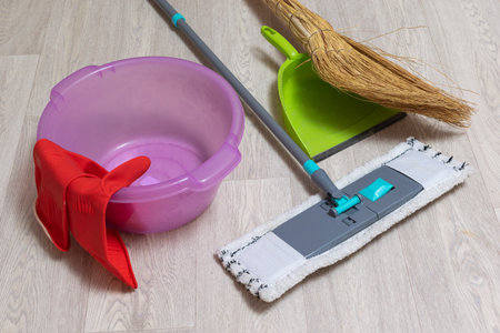 Home Cleaning Essentials: Mop, Bucket, Dustpan, Broom, and Rubber Gloves on Wooden Floorの写真素材