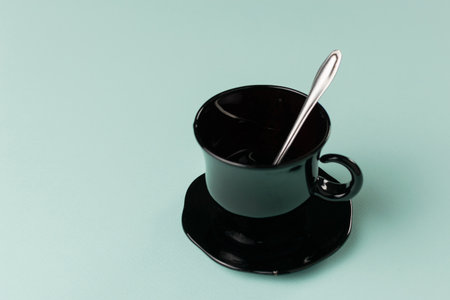 Minimalist Black Coffee Cup with Spoon on Soft Teal Background Reflecting Modern Elegance