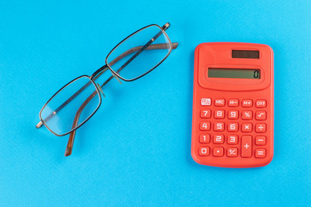 Red Calculator and Glasses on Blue Background: Modern Office Essentials and Business Conceptsの写真素材