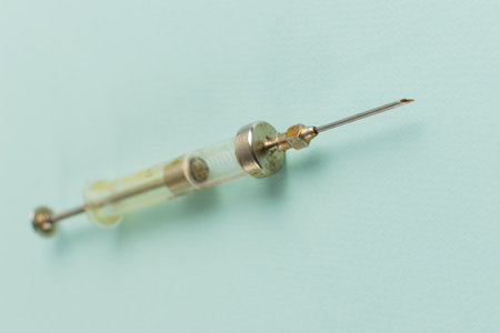 Vintage Glass Syringe with Needle Against Light Blue Background Reflecting Medical Historyの写真素材
