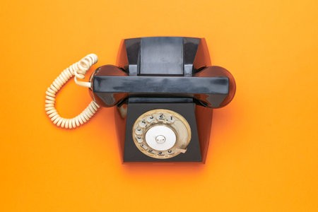 Vintage Black Rotary Telephone on Vibrant Orange Background for Retro Communication Themesの写真素材