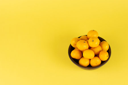 Fresh Kumquats in a Bowl on Vibrant Yellow Background Highlighting Citrus Brightness