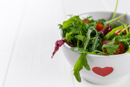 Fresh Mixed Green Salad in Heart Bowl on White Backgroundの写真素材