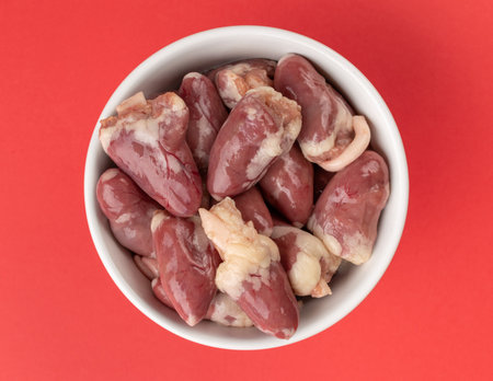 Raw Chicken Hearts in White Bowl on Vibrant Red Backgroundの写真素材