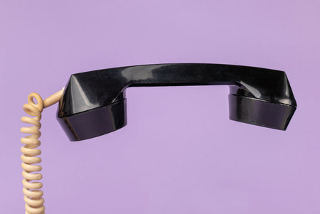 Vintage Black Telephone Handset with Coiled Cord on Pastel Purple Backgroundの写真素材