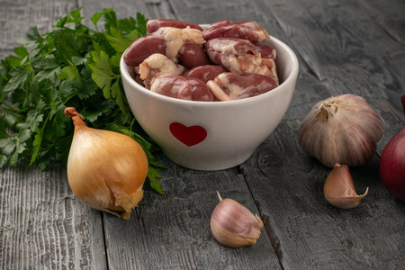 Fresh Chicken Hearts, Garlic, Onions, and Herbs on Rustic Wooden Tableの写真素材