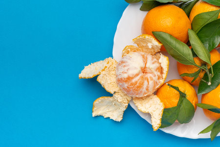 Fresh Tangerines with Leaves on White Plate Against Vibrant Blue Backgroundの写真素材