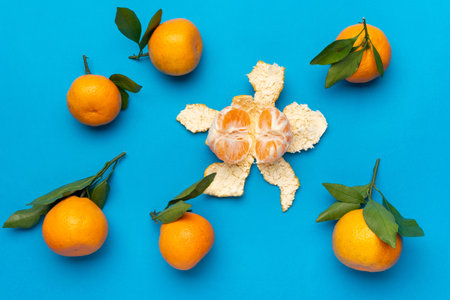 Fresh Oranges with Leaves and Peeled Mandarin on Vibrant Blue Backgroundの写真素材