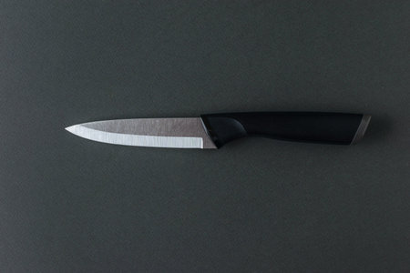 A kitchen knife with a black handle and a metal blade on a gray background.の写真素材