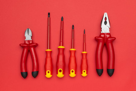 Red Insulated Hand Tools on Red Background: Pliers and Screwdrivers for Electrical Work
