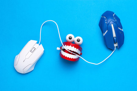 Playful Tech Battle: Toy Teeth Tug-of-War with Wired Computer Mice on Blue Background