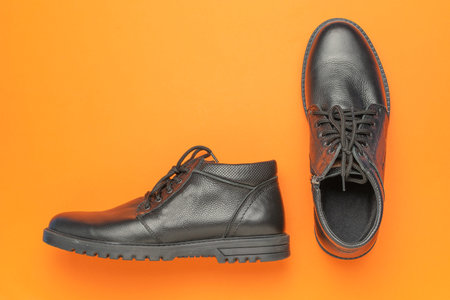 Black Leather Boots on Vibrant Orange Background: Modern Footwear Aesthetic