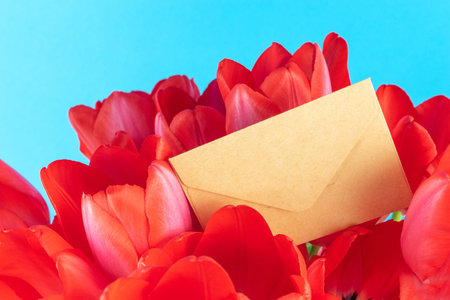 Brown Envelope Amidst Vibrant Red Tulips Against a Bright Blue Background