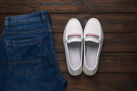 Trendy White Loafers Paired with Denim Jeans on Rustic Wooden Surface for Fashion Concept