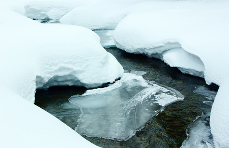 Rocky stream flowing among the snowdrifts.Tinted image.の写真素材