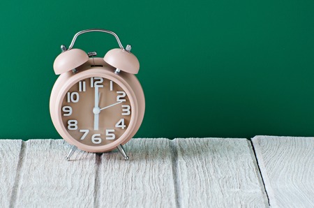 brown clock on wooden table with green backgroundの写真素材