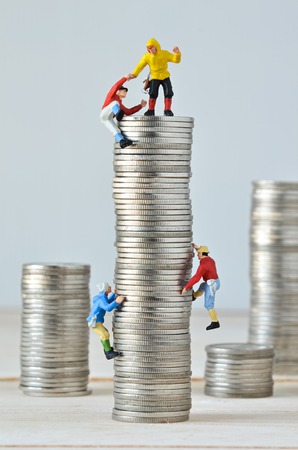 Miniature climbers team climbing on stack of coinsの写真素材