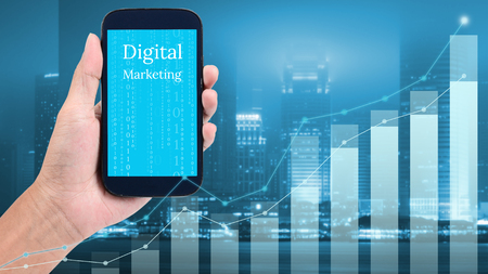 Man hand holding mobile phone for digital marketing with graph and city backgroundの写真素材
