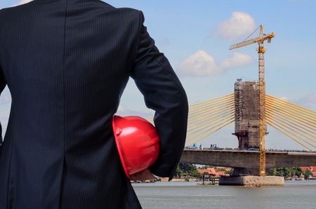 business man holding red safety helmet with construction site backgroundの写真素材