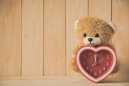 teddy bear holding red heart clock on wooden tableの写真素材