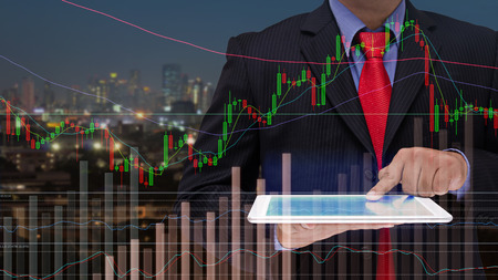 business man using tablet with graph on screen and modern night city backgroundの写真素材