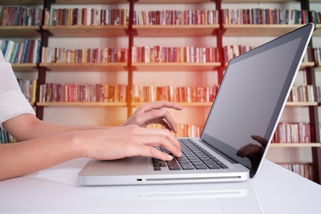 woman hand using laptop on white table with book shelf background