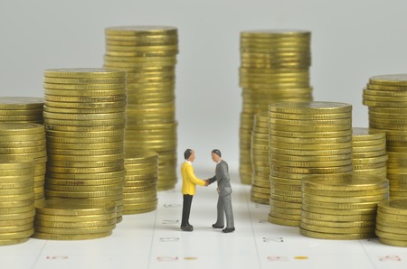 miniature people agreement with stack of coins and calendar backgroundの写真素材