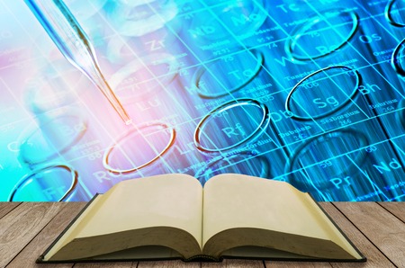 open book on wooden table with science laboratory test tubes background