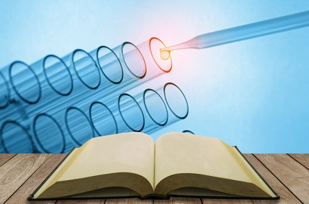 open book on wooden table with science laboratory test tubes background