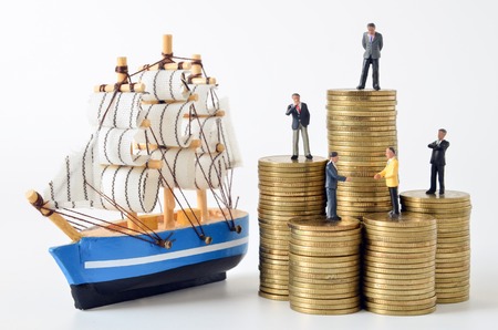 business miniature people on stack of coins and sailboat modelの写真素材